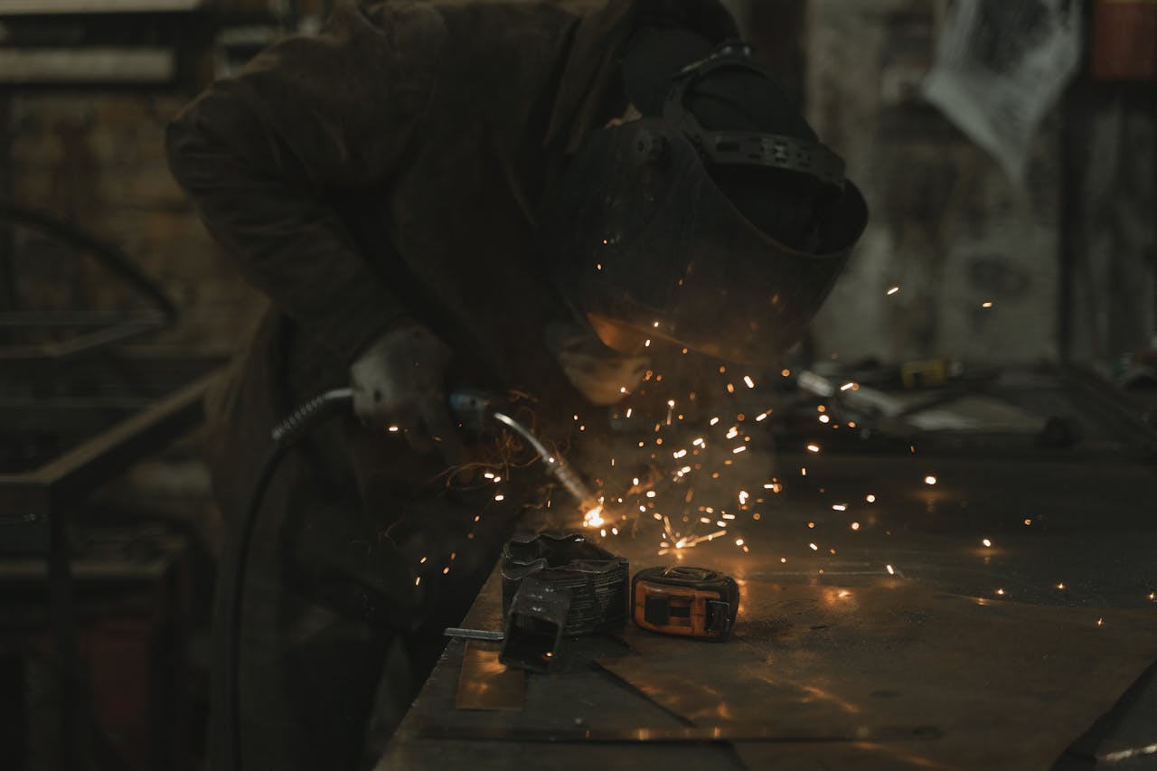 services-03 A welder skillfully operates in a dimly lit workshop, surrounded by sparks.