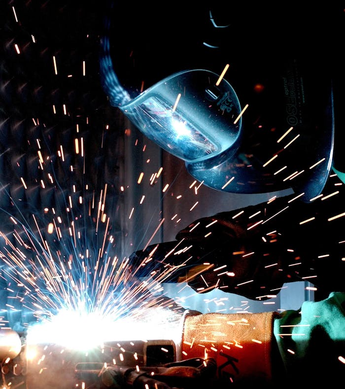 services-01 A focused welder works with metal in an industrial setting, creating vibrant sparks.